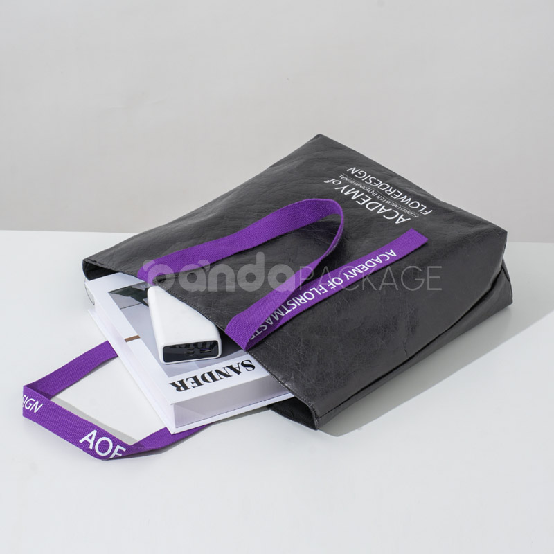 black paper tote bag with purple woven logo handles