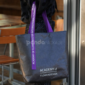black paper tote bag with purple woven logo handles