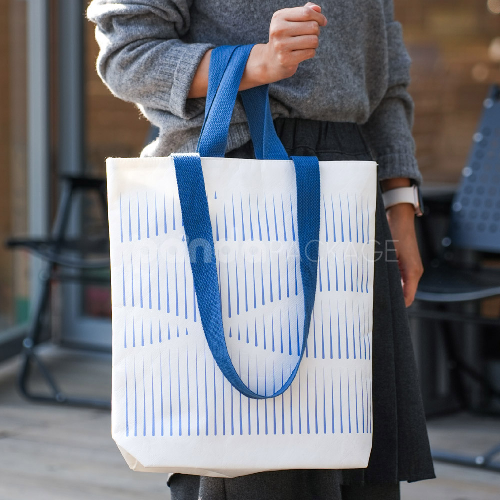 Ivory tote bag with blue woven handles and abstract line pattern