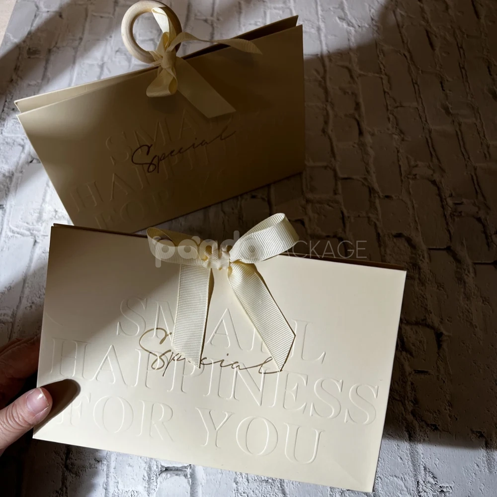 luxury cream paper gift bag with embossed text and ribbon bow