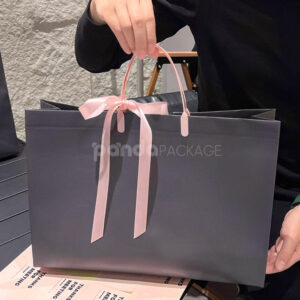 laminated non-woven tote bags with plastic handles and ribbon bow for apparel packaging in customizable colors and sizes