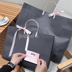 laminated non-woven tote bags with plastic handles and ribbon bow for apparel packaging in customizable colors and sizes