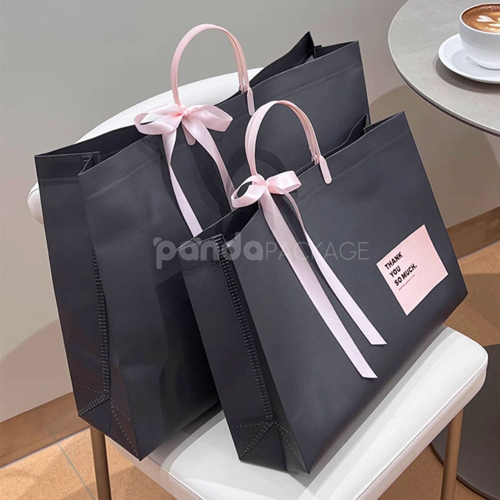 laminated non-woven tote bags with plastic handles and ribbon bow for apparel packaging in customizable colors and sizes