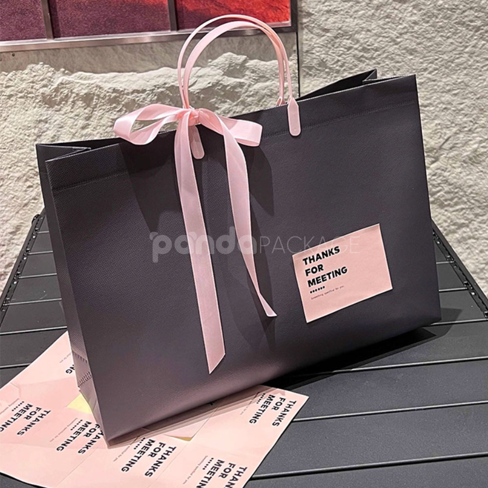 laminated non-woven tote bags with plastic handles and ribbon bow for apparel packaging in customizable colors and sizes