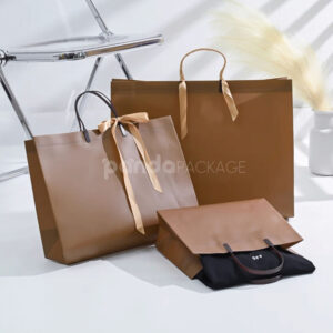 laminated non-woven tote bags with plastic handles and ribbon bow for apparel packaging in customizable colors and sizes
