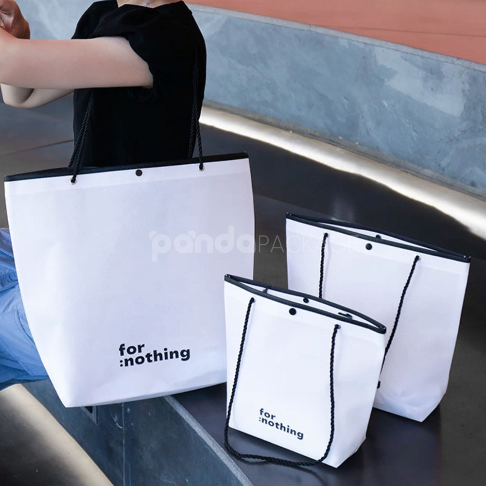 tapered non-woven tote bags with rope handles and piping edges, available in multiple colors and custom sizes for apparel packaging