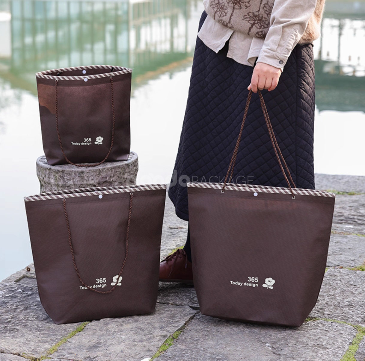 tapered non-woven tote bags with rope handles and piping edges, available in multiple colors and custom sizes for apparel packaging