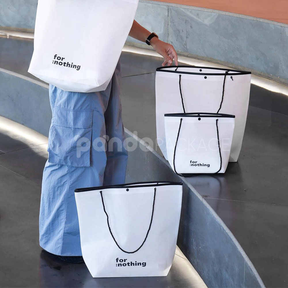 tapered non-woven tote bags with rope handles and piping edges, available in multiple colors and custom sizes for apparel packaging